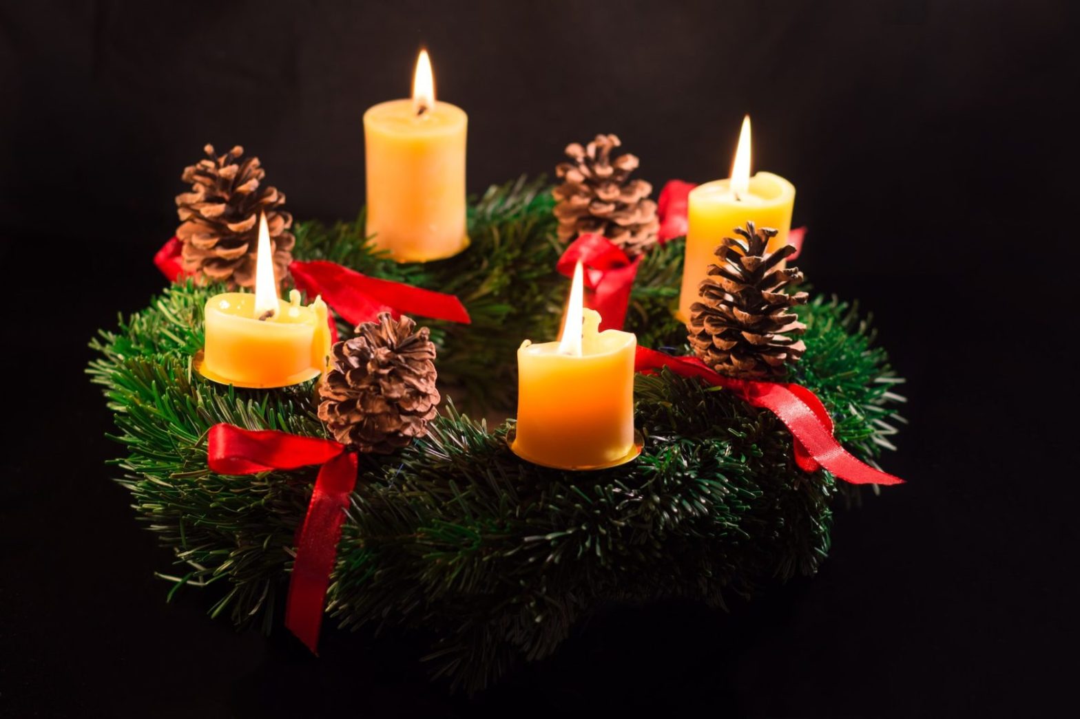 a group of lit candles sitting on top of a christmas wreath