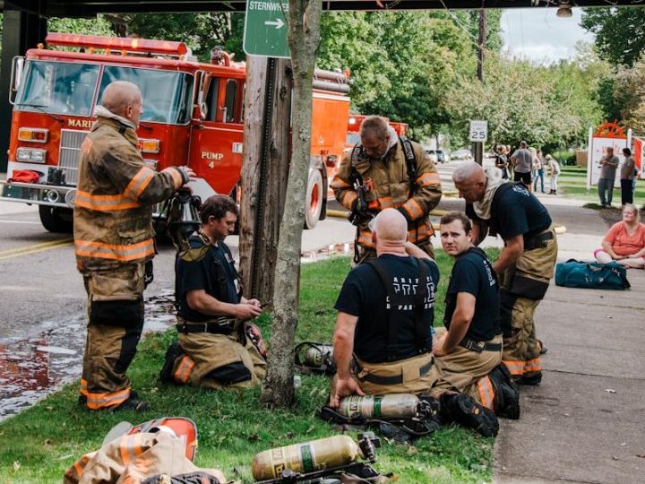 a group of firemen sitting on the ground next to a tree