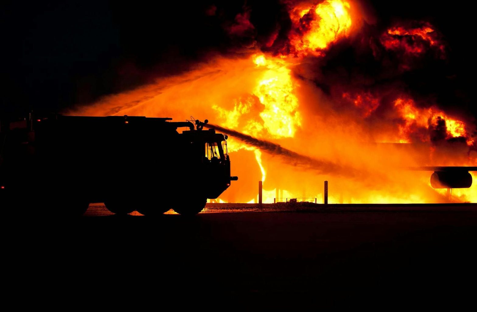 Dramatic image of a fire truck silhouette against a massive blaze, showcasing emergency response.