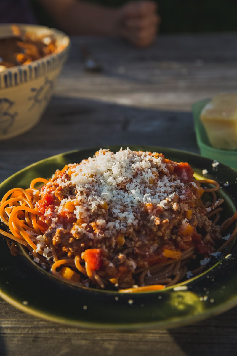 Delicious spaghetti Bolognese topped with grated Parmesan cheese served on a rustic outdoor table.